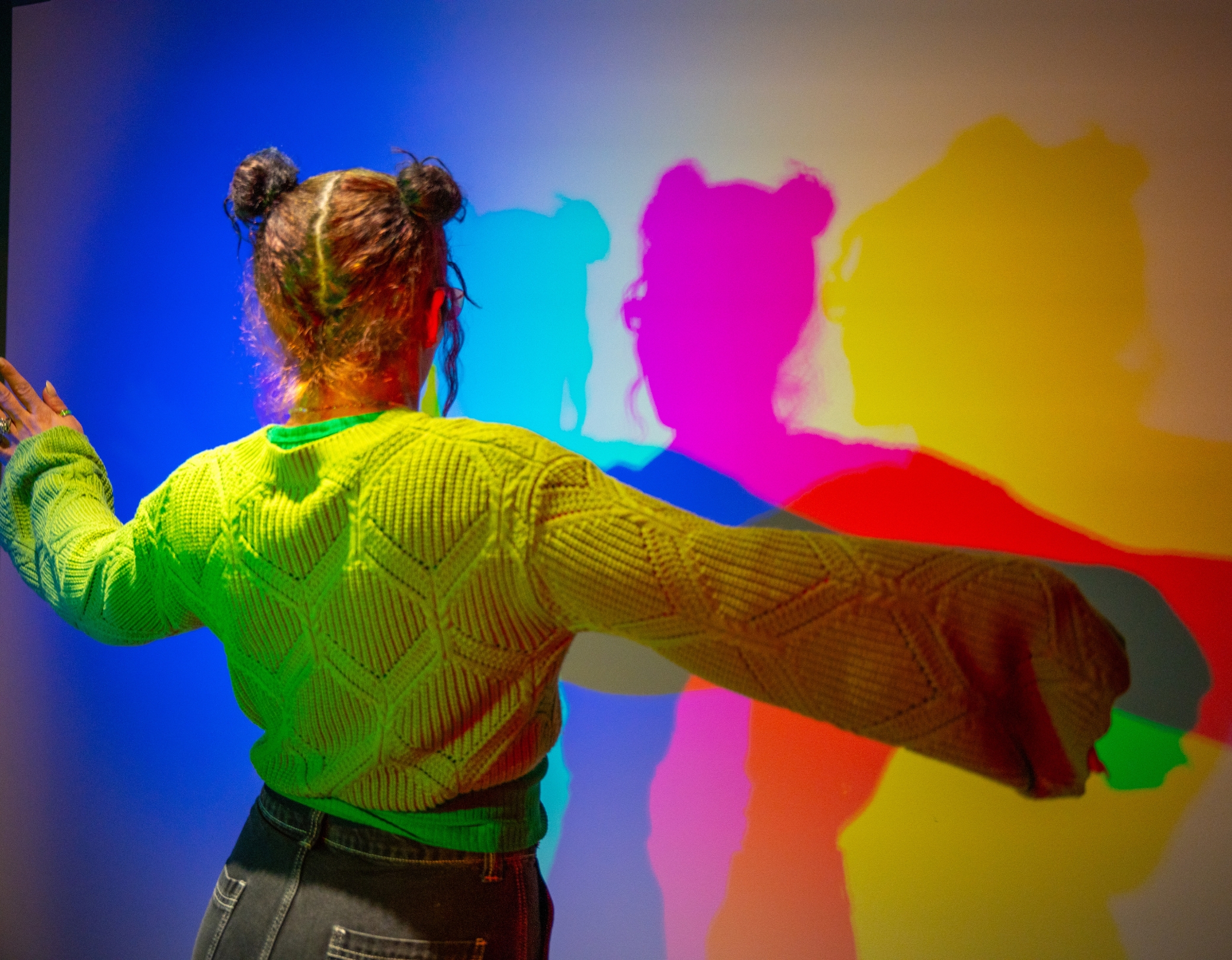 Mädchen im Color Room des Museum der Illusionen Hamburg erzeugt farbige Schatten durch Lichtprojektion in Rot, Grün und Blau