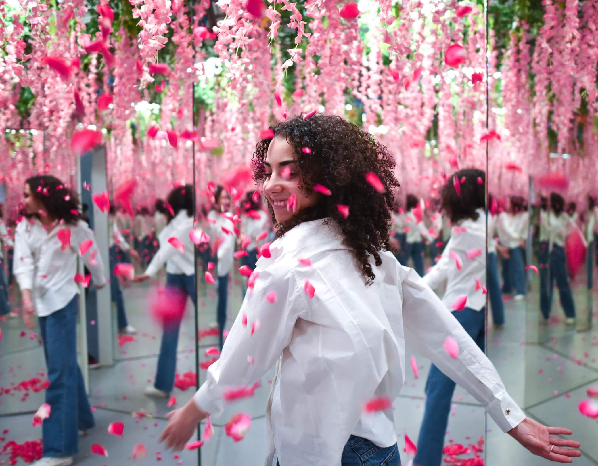 Frau tanzt durch einen mit Spiegeln und rosa Blüten dekorierten Infinity Room im Museum der Illusionen Hamburg