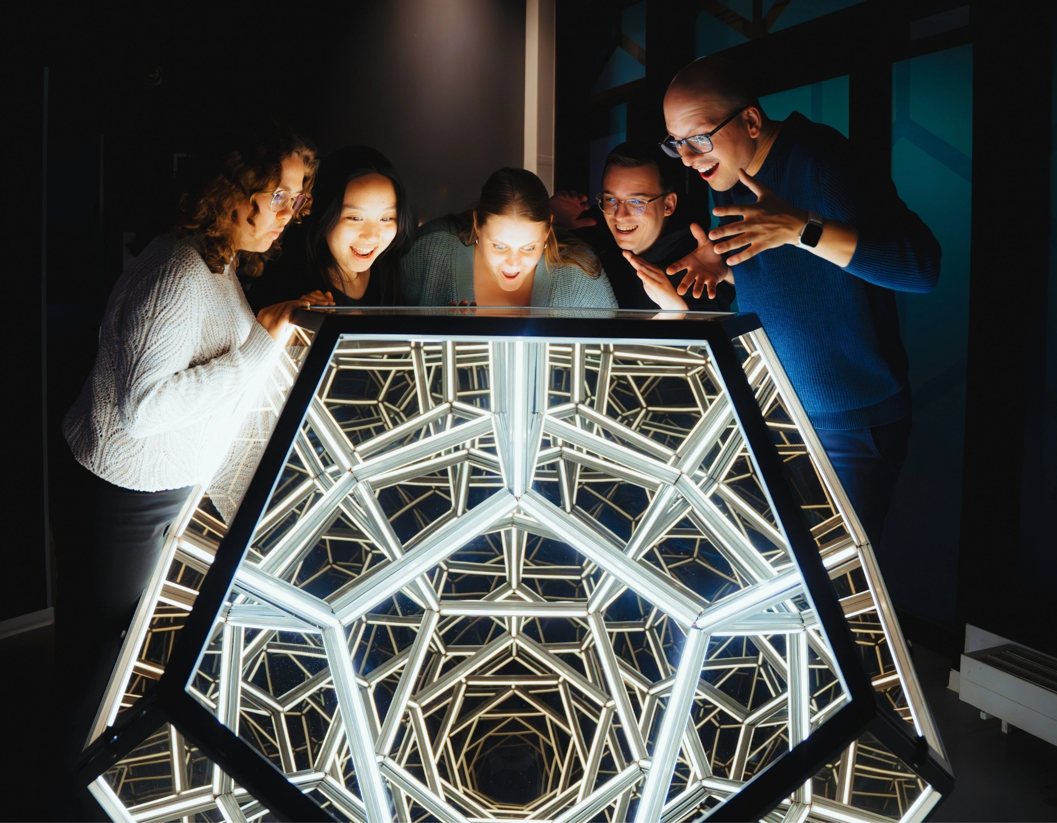 Gruppe junger Menschen staunt über ein leuchtendes, spiegelndes Dodekaeder im Museum der Illusionen Hamburg