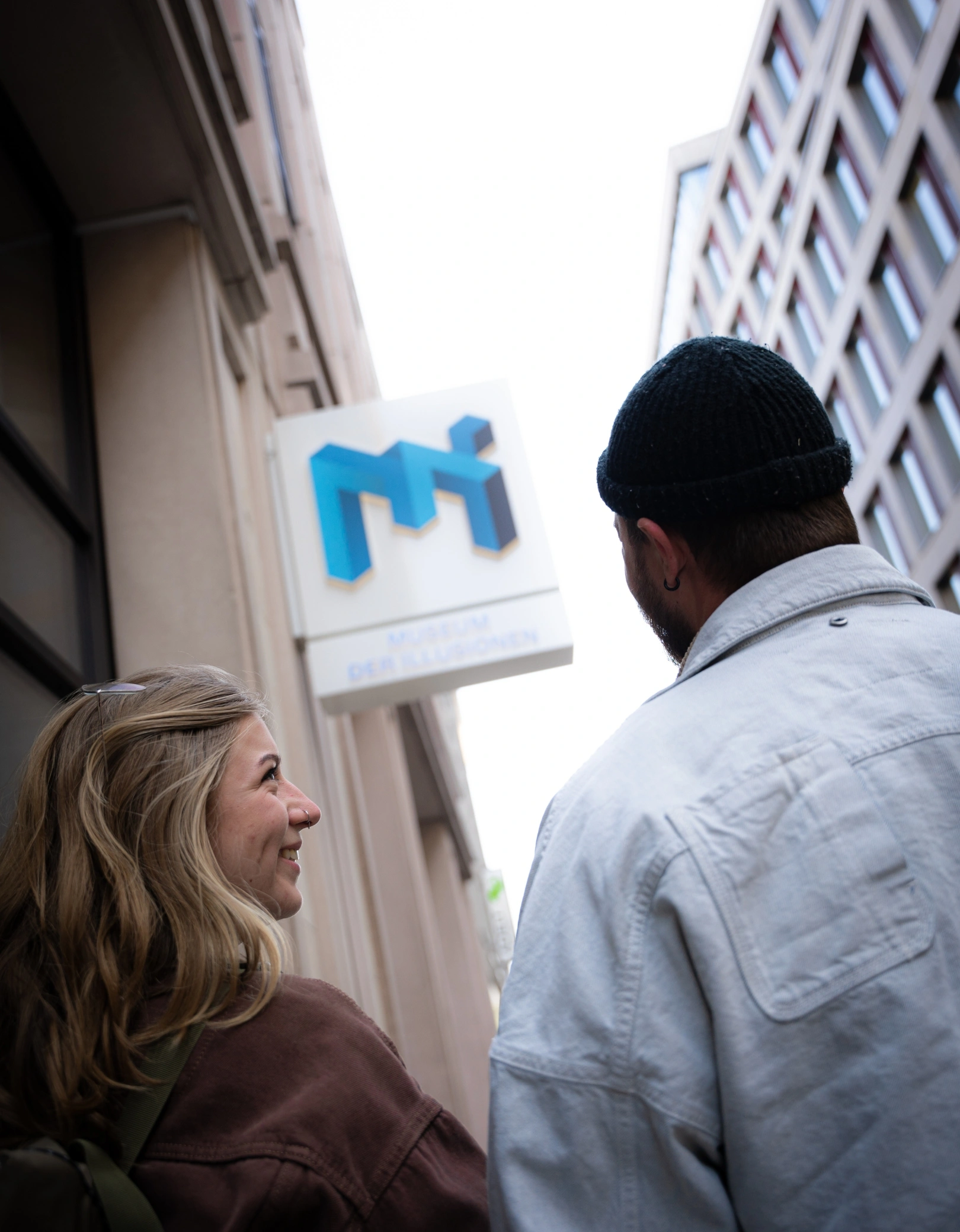 Ein Paar steht vor dem Eingang des Museum der Illusionen Hamburg und blickt auf das Museumslogo über der Tür.
