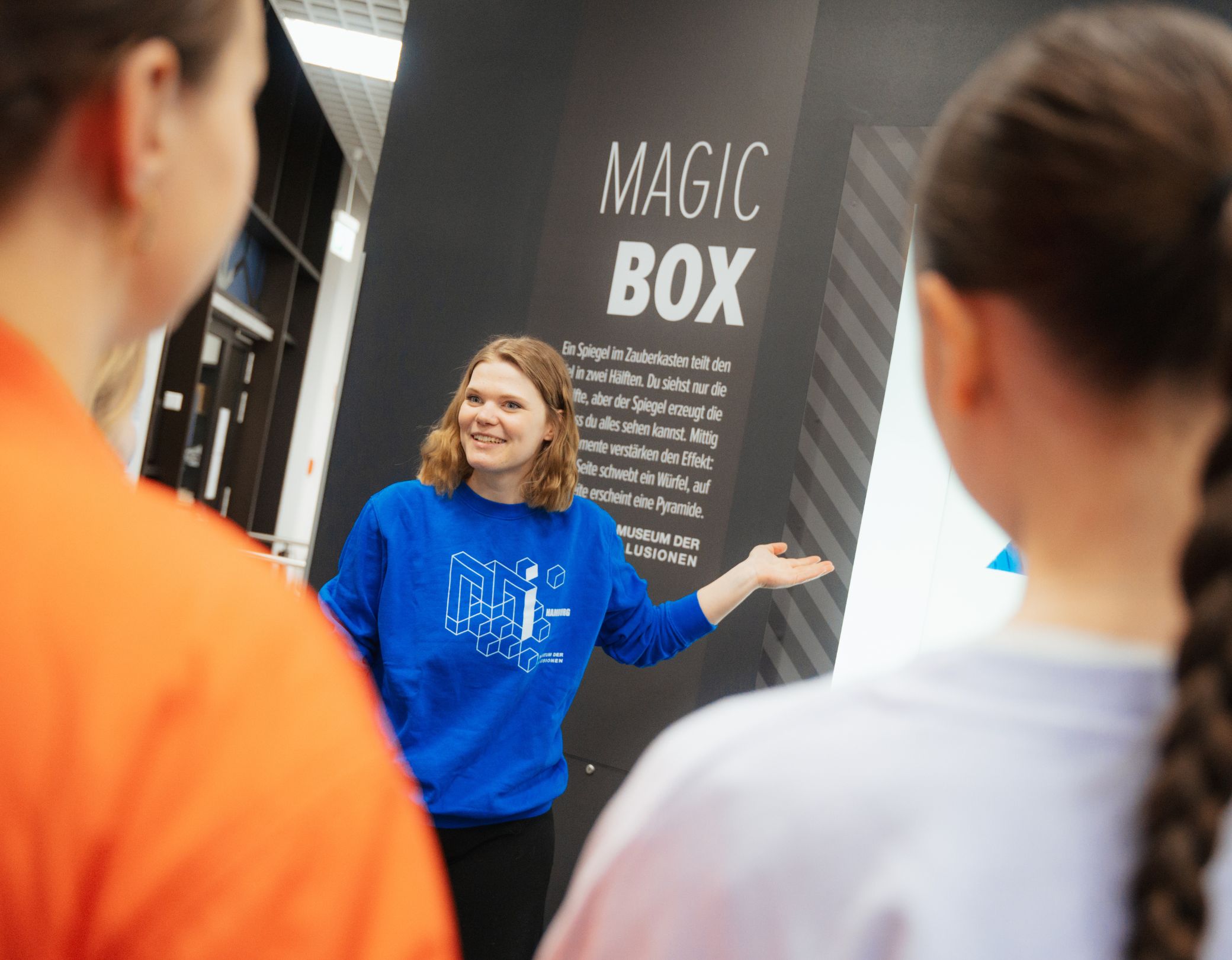 Eine Mitarbeiterin erklärt einer Gruppe von Frauen ein Exponat im Museum der Illusionen