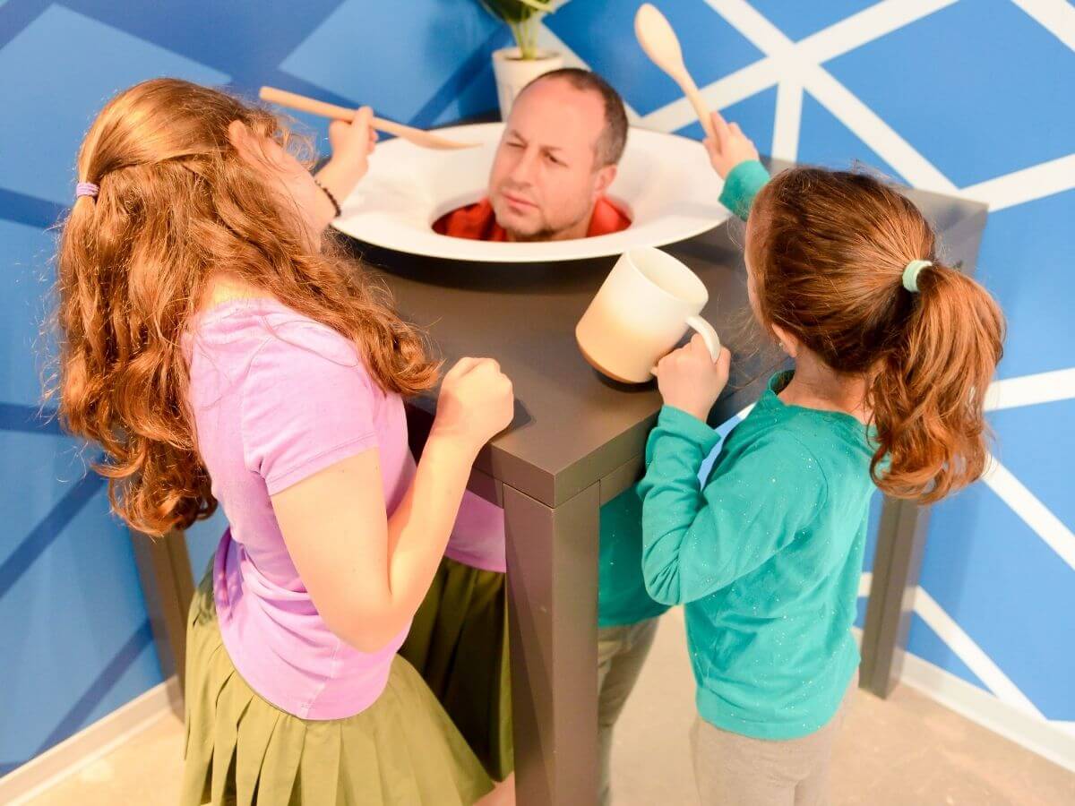 Kinder haben zusammen mit ihrem Vater Spaß beim Ausprobieren einer lustigen Illusion im Museum der Illusionen Hamburg