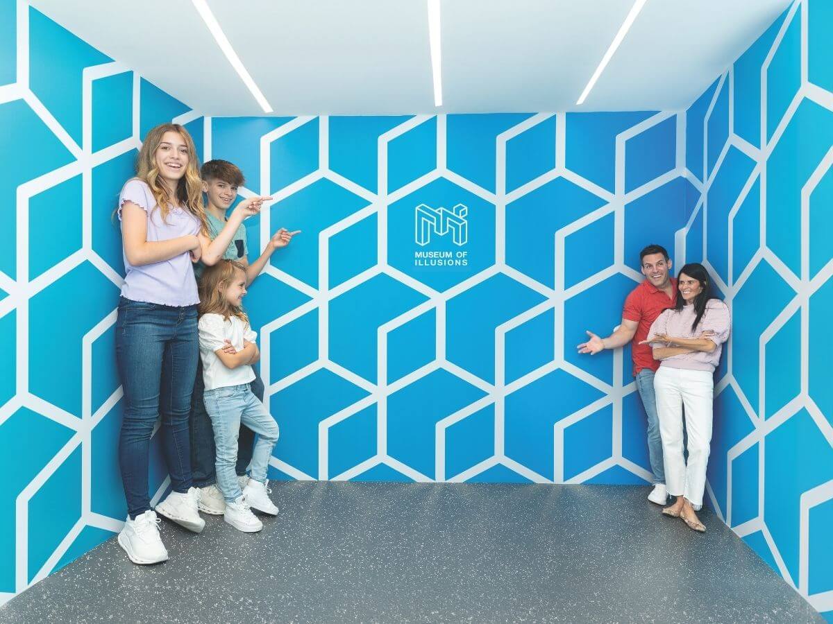 Eine Familie steht im Ames Raum im Museum der Illusionen. Durch die Größenverzerrung wirken die Kinder größer als die Erwachsenen.